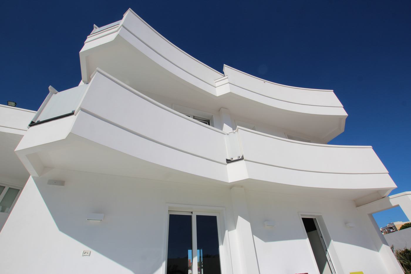 Casa M: balconi curvi bianchi sovrapposti, visti dal basso contro il cielo